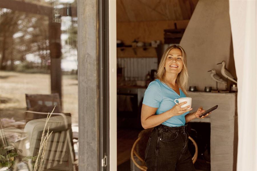 Vrouw staat in de deur opening met kop thee in haar hand